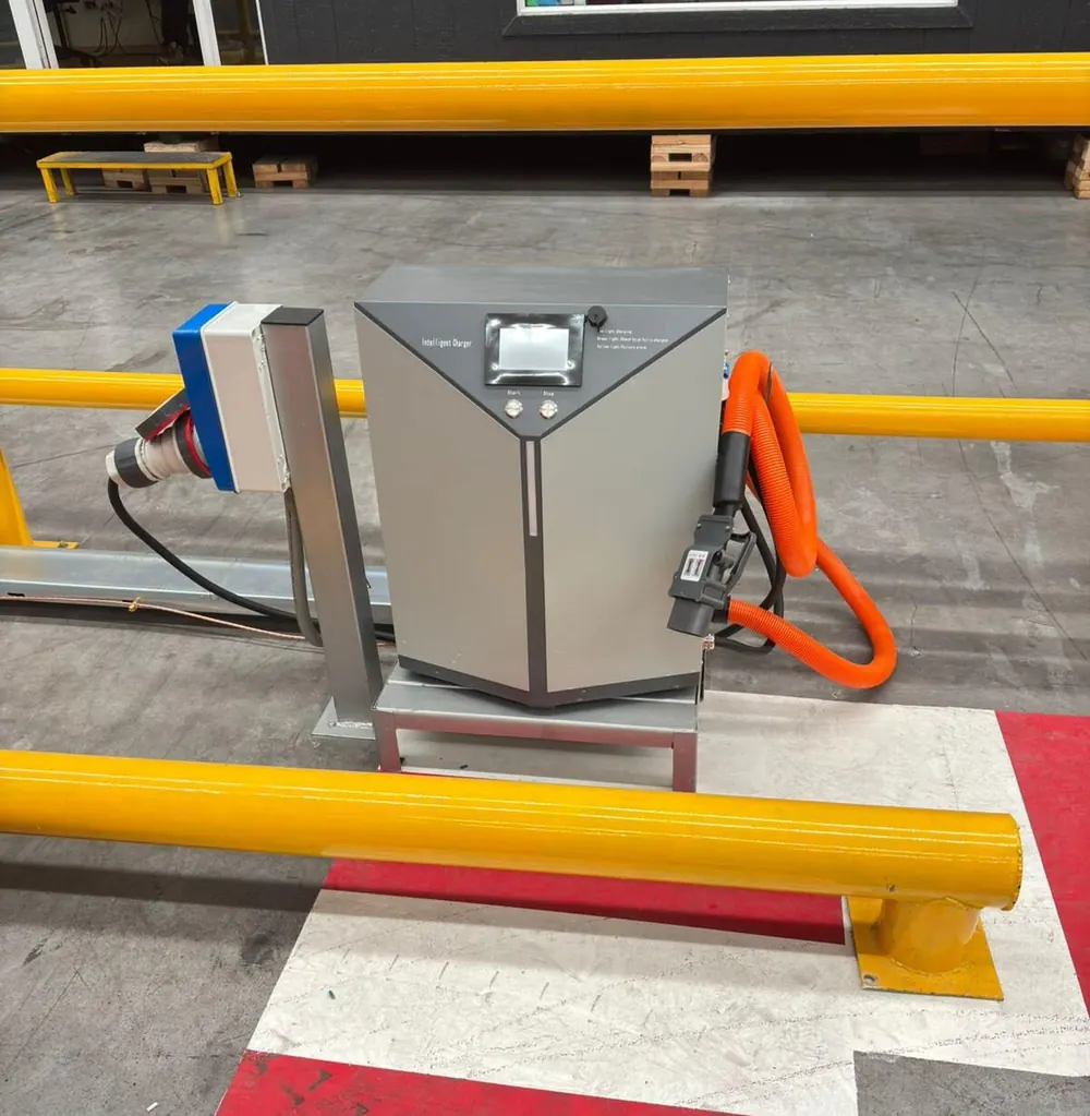 Cargador industrial de baterías para grúa horquilla instalado en bodega, con barandas amarillas de protección